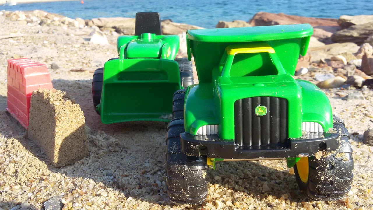 Грейдер и самосвал строят замок из песка. Vehicles on the beach